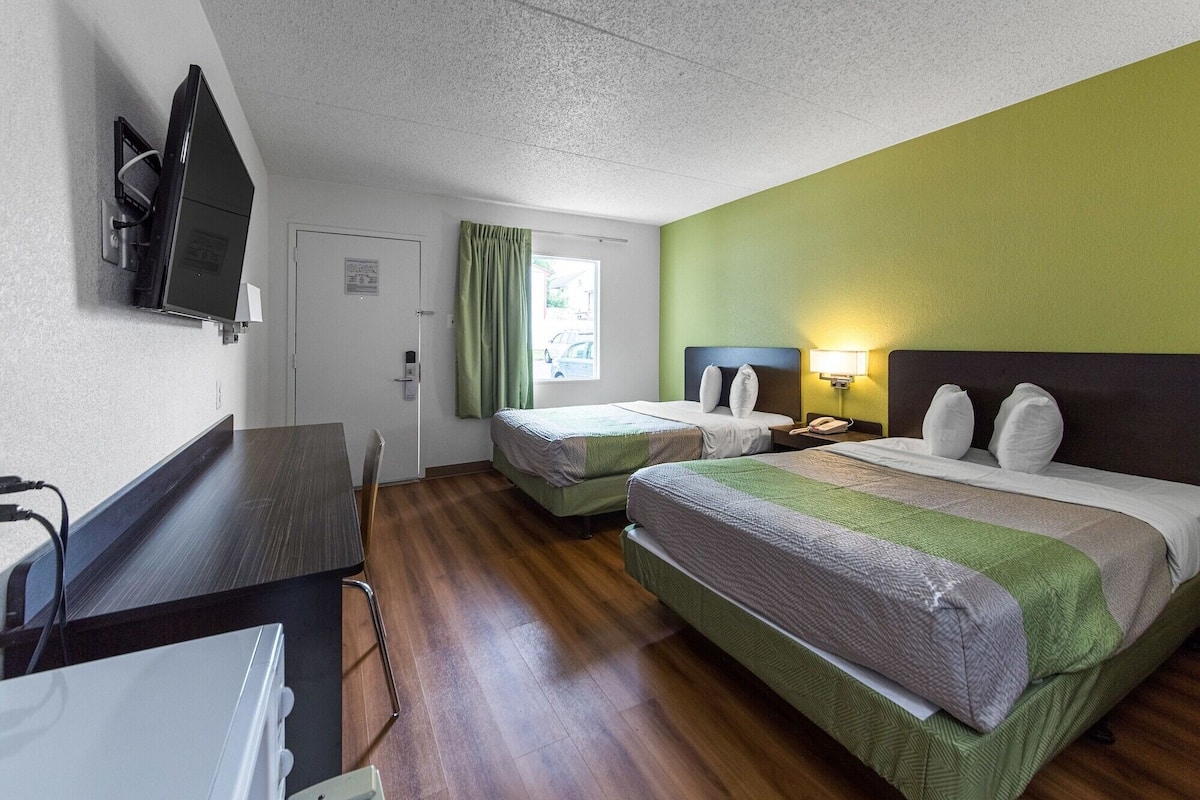A hotel room with two single beds, a desk, a television, and a window with curtains.