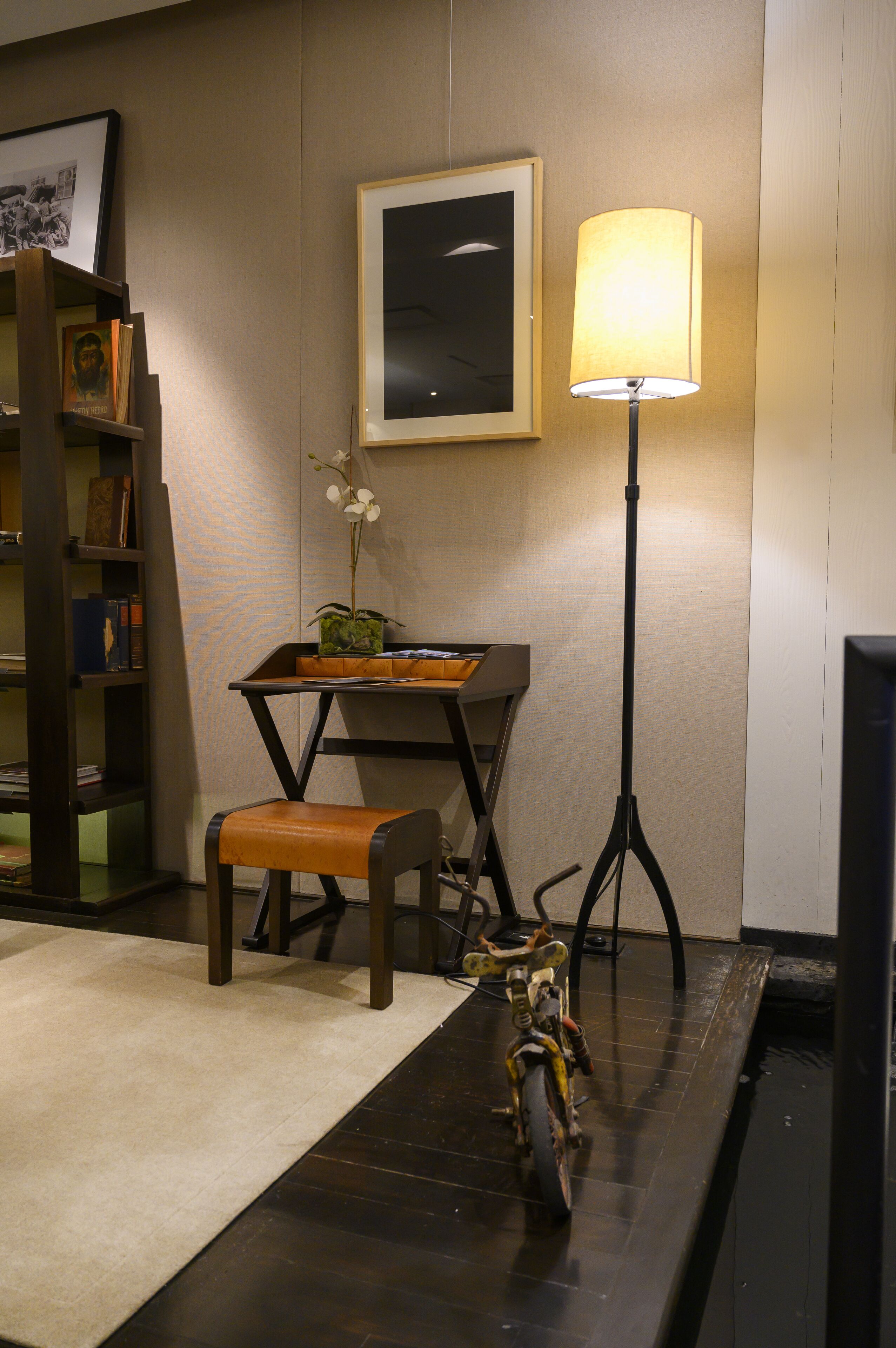 A room with a desk, chair, lamp, bookshelf, and a motorcycle.
