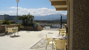 Una terraza al aire libre con sillas y mesas amarillas, un farol y vistas a una cordillera.