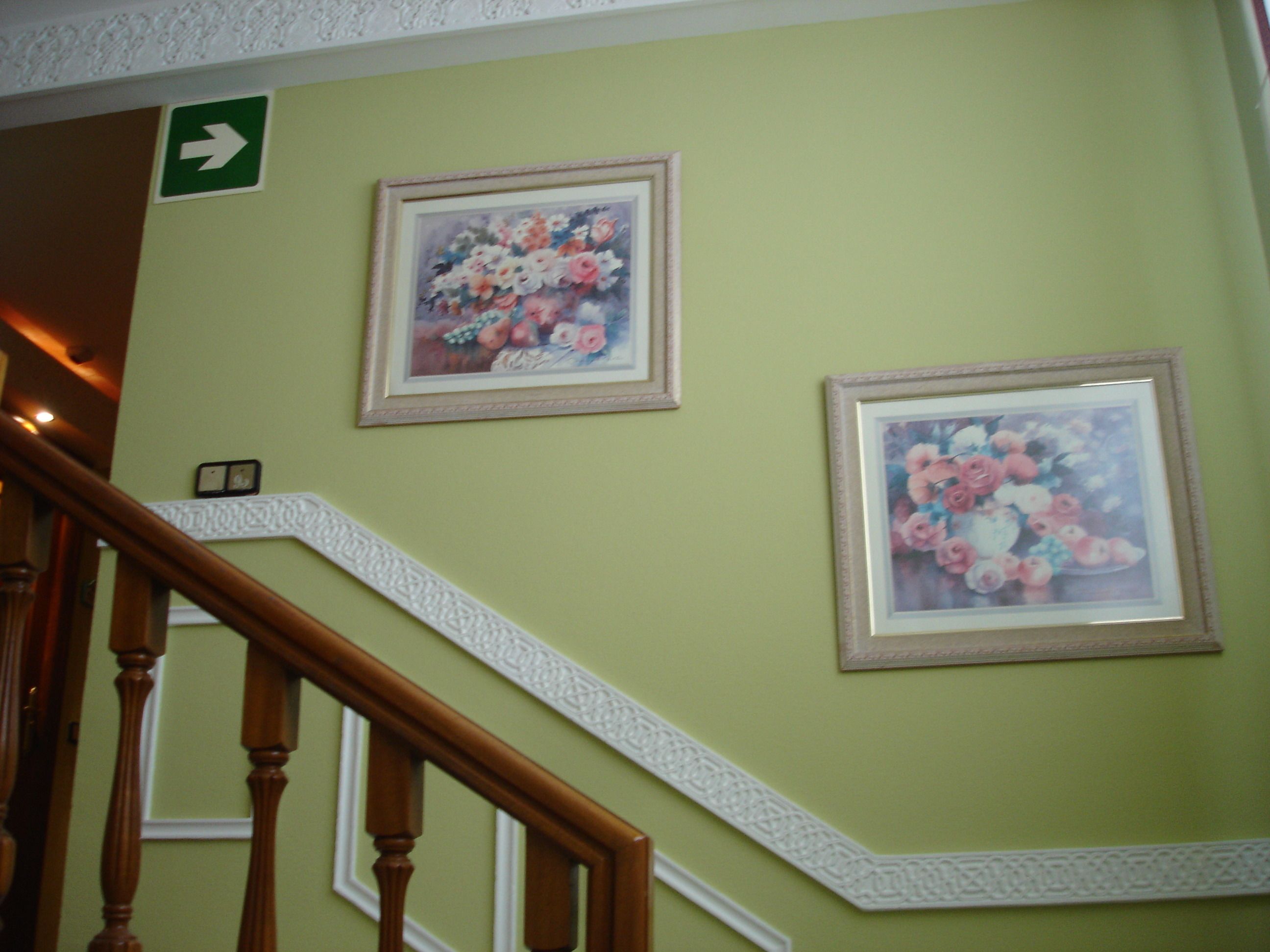 A staircase with a wooden handrail and a green wall with two framed floral paintings.