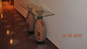 Un pasillo con una mesa de vidrio, dos jarrones decorativos y lámparas de pared.