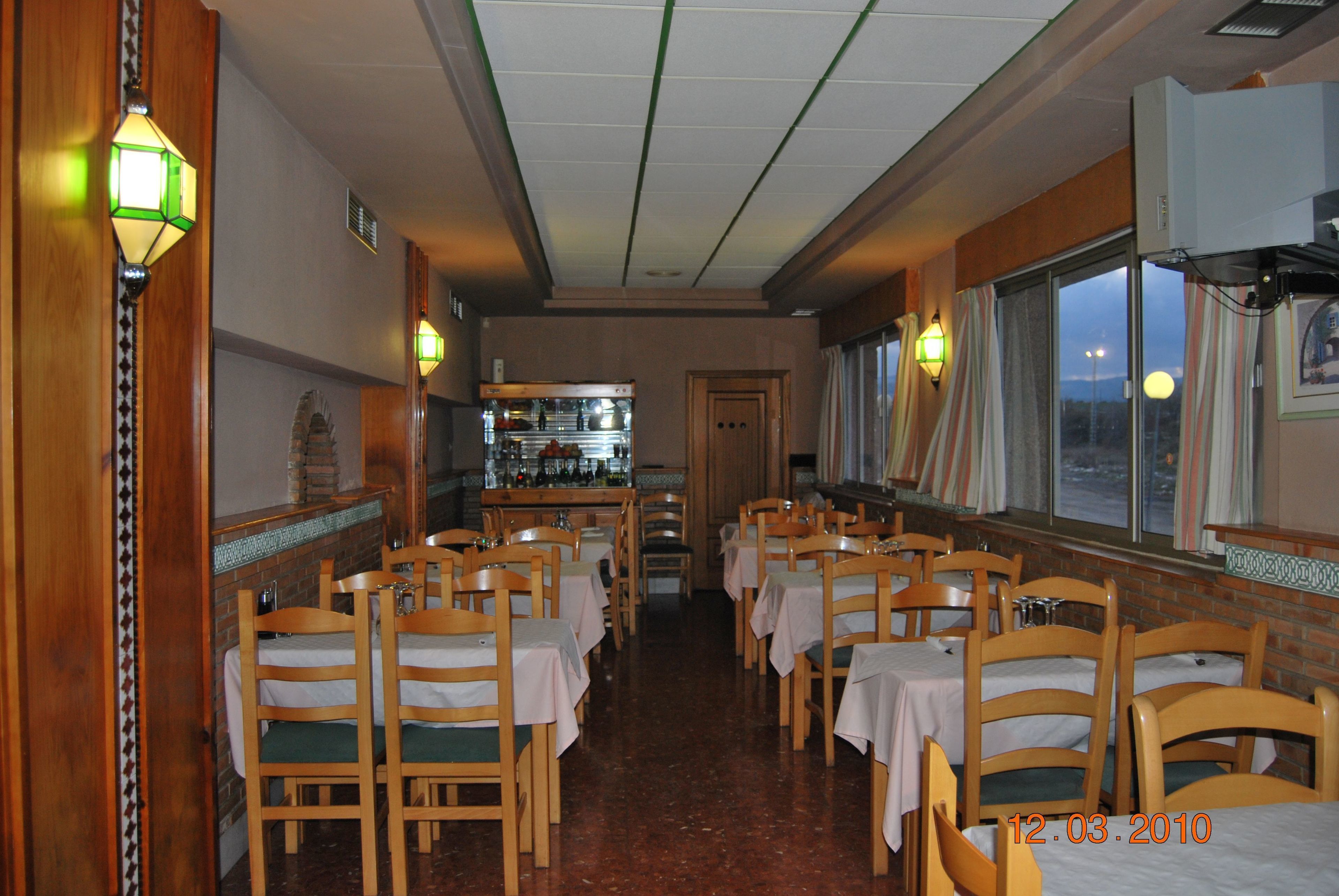 A restaurant with wooden chairs and tables, a bar area, and large windows.