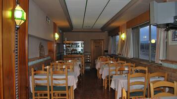 A restaurant with wooden chairs and tables, a bar area, and large windows.