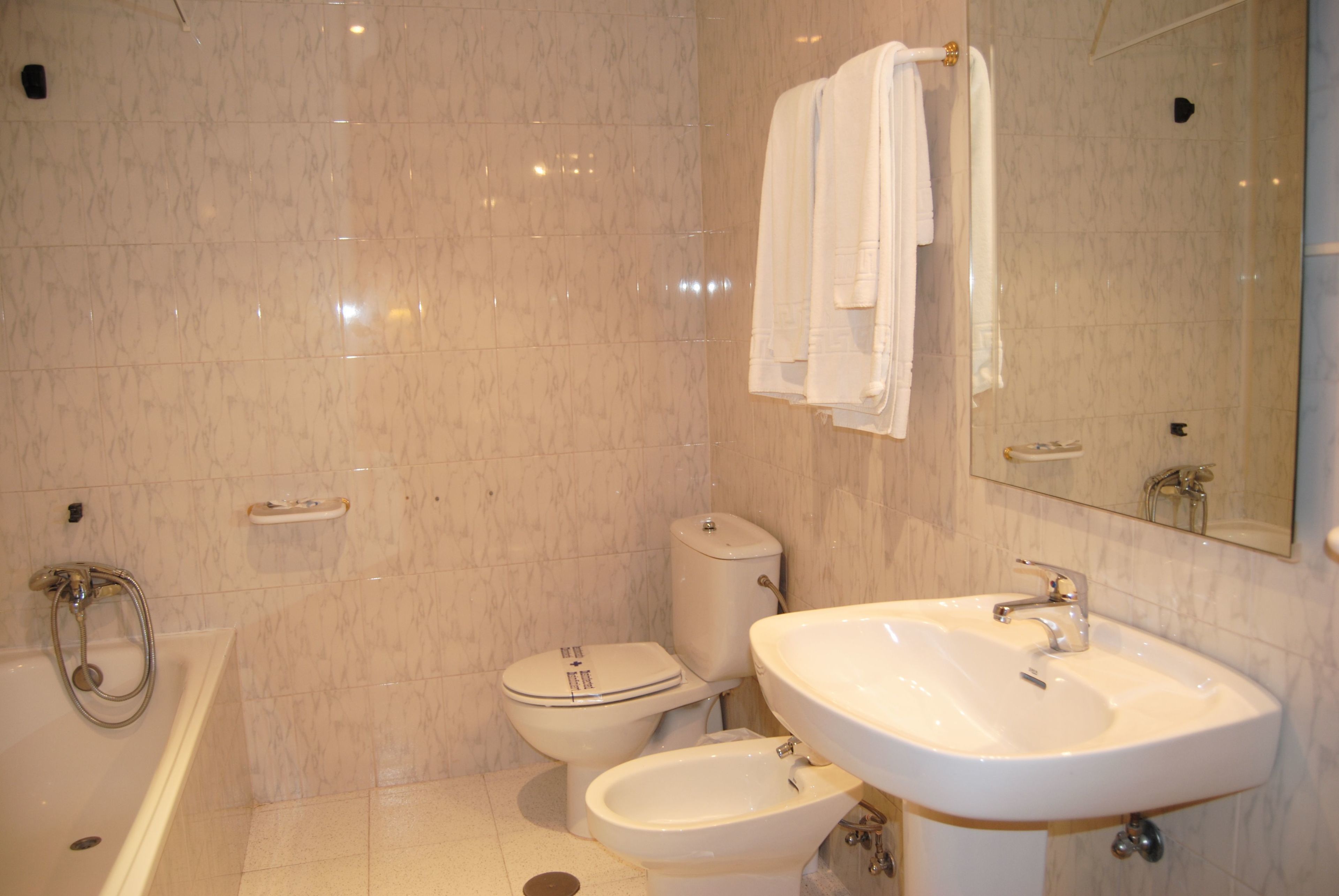 Une salle de bain équipée d’une baignoire, de toilettes, d’un bidet, d’un lavabo et d’un grand miroir.