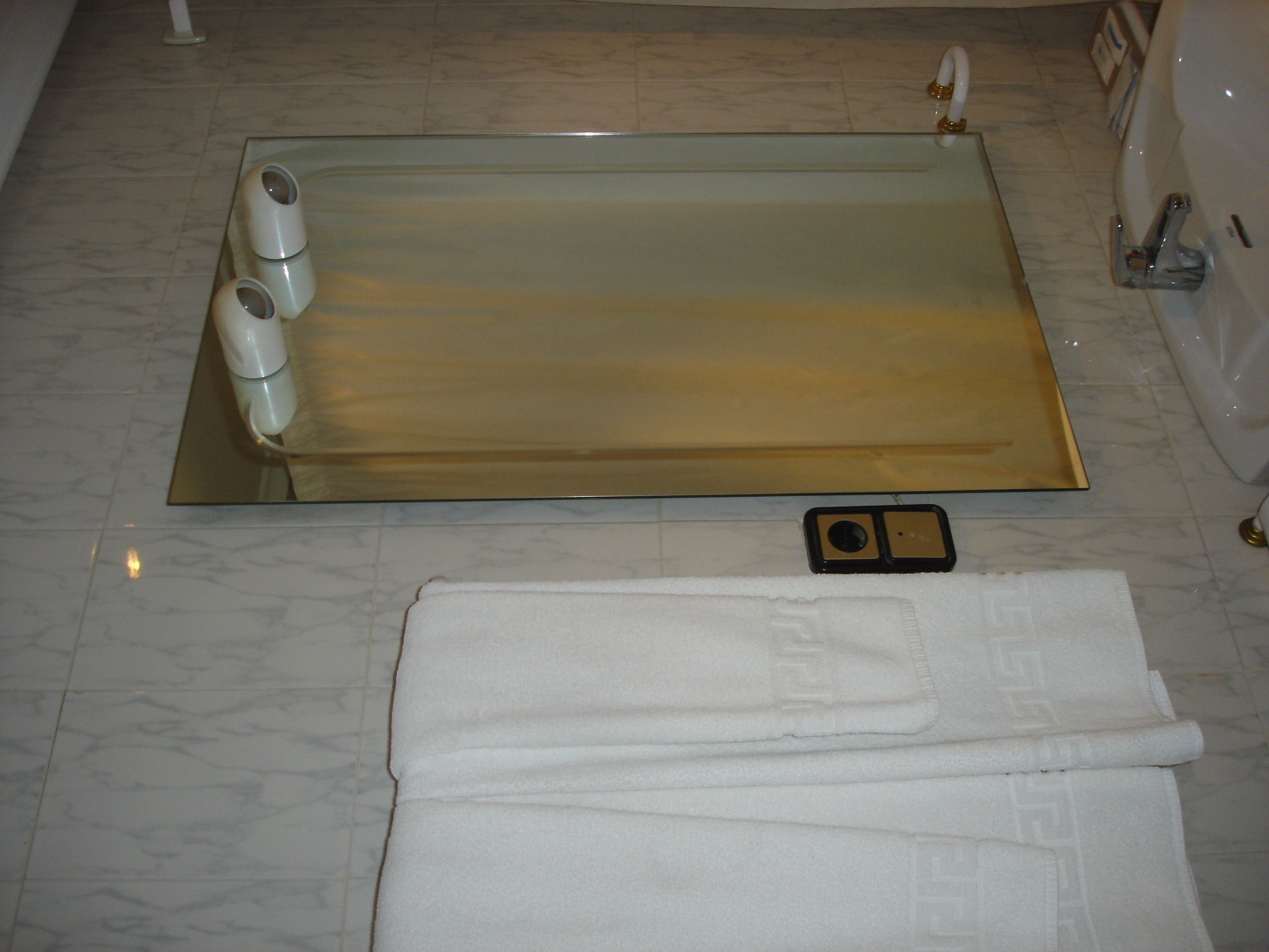 Un baño con una bañera de vidrio, una toalla blanca y un cabezal de ducha de mano.