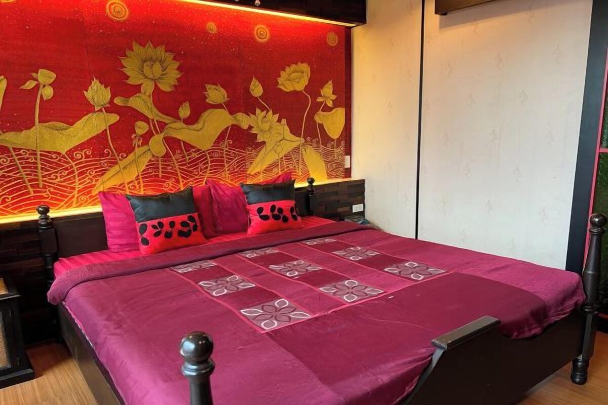 Una cama con una colcha estampada en rojo y negro, dos almohadas con diseños negros y rojos, y una pared con un mural floral.