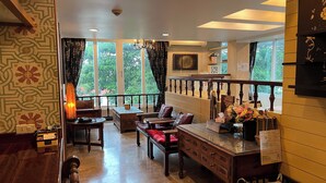 A spacious room with a wooden bench, a table with a vase of flowers, and a view of greenery through large windows. - Sabai Sabai @ Sukhumvit Hotel (Bangkok)