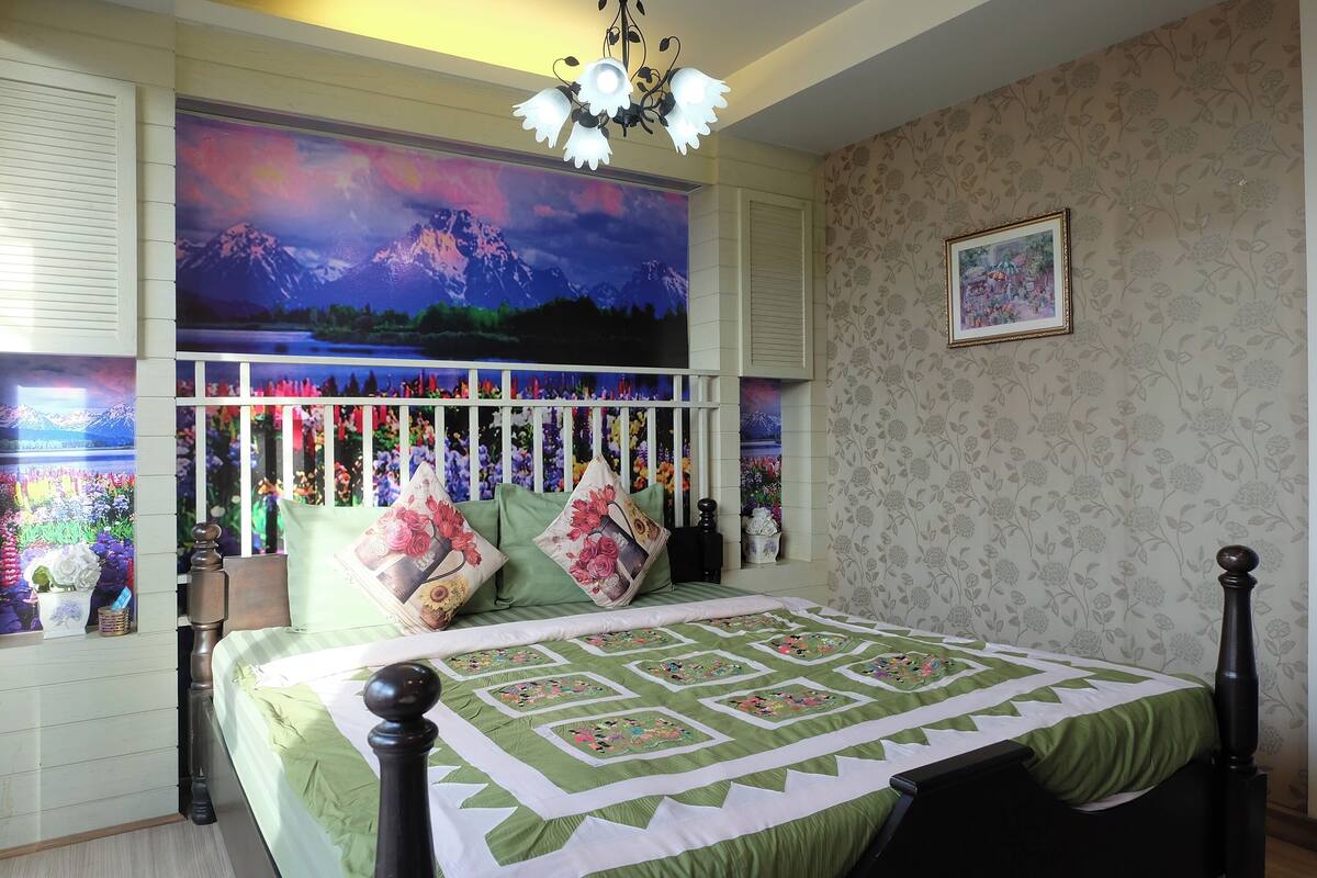 Une chambre à coucher avec un grand lit, une tête de lit décorative, un mur orné d’un motif floral et un tableau encadré.
