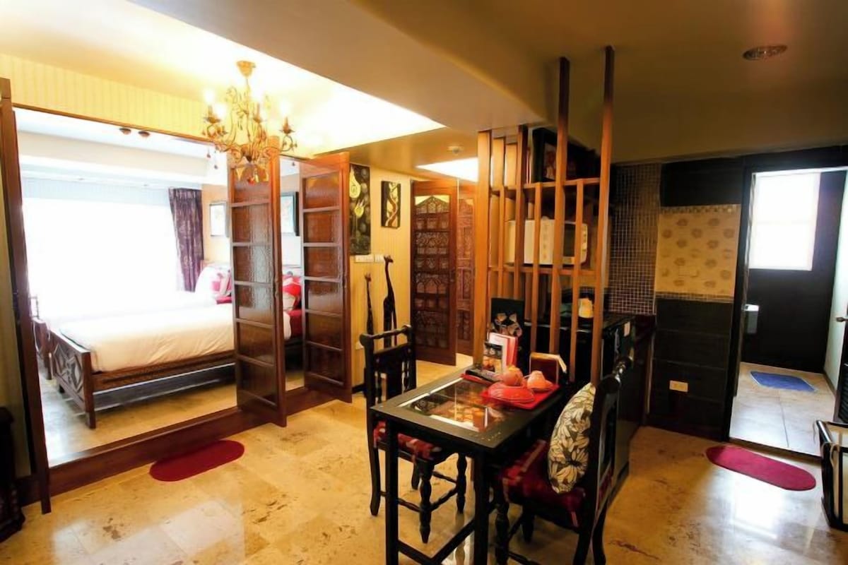 A room with a bed, a dining table, chairs, a chandelier, and a sliding door leading to another room.