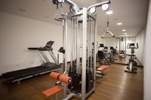 Une salle de sport équipée de tapis de course, d’appareils de musculation et de bancs.