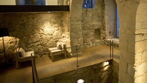 A stone-walled interior with a wooden bench and a table, a glass railing, and a lamp. - Hotel Carris Porto Ribeira (Porto)