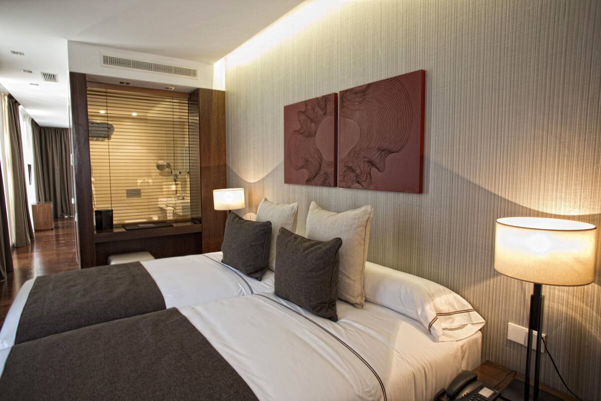 A hotel room with a large bed, two bedside tables, a lamp, and a wall-mounted artwork.