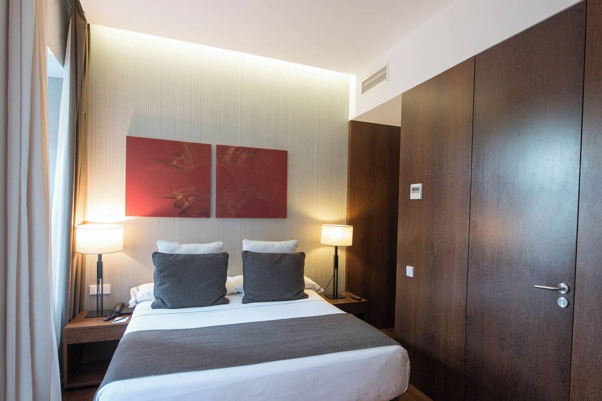 A hotel room with a large bed, two bedside lamps, a nightstand, and a wardrobe.