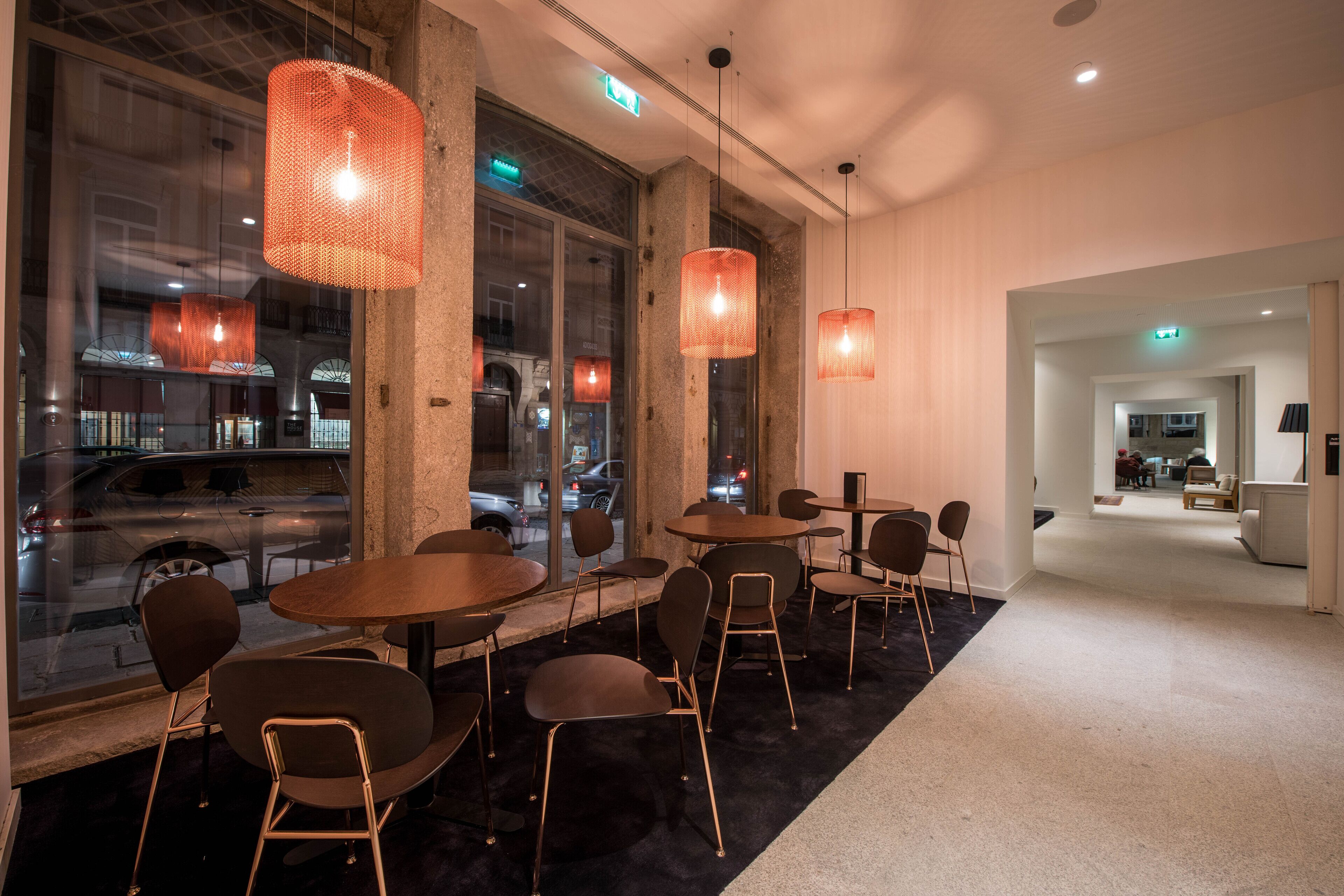 A modern interior with round tables and chairs, large windows, and hanging orange pendant lights.