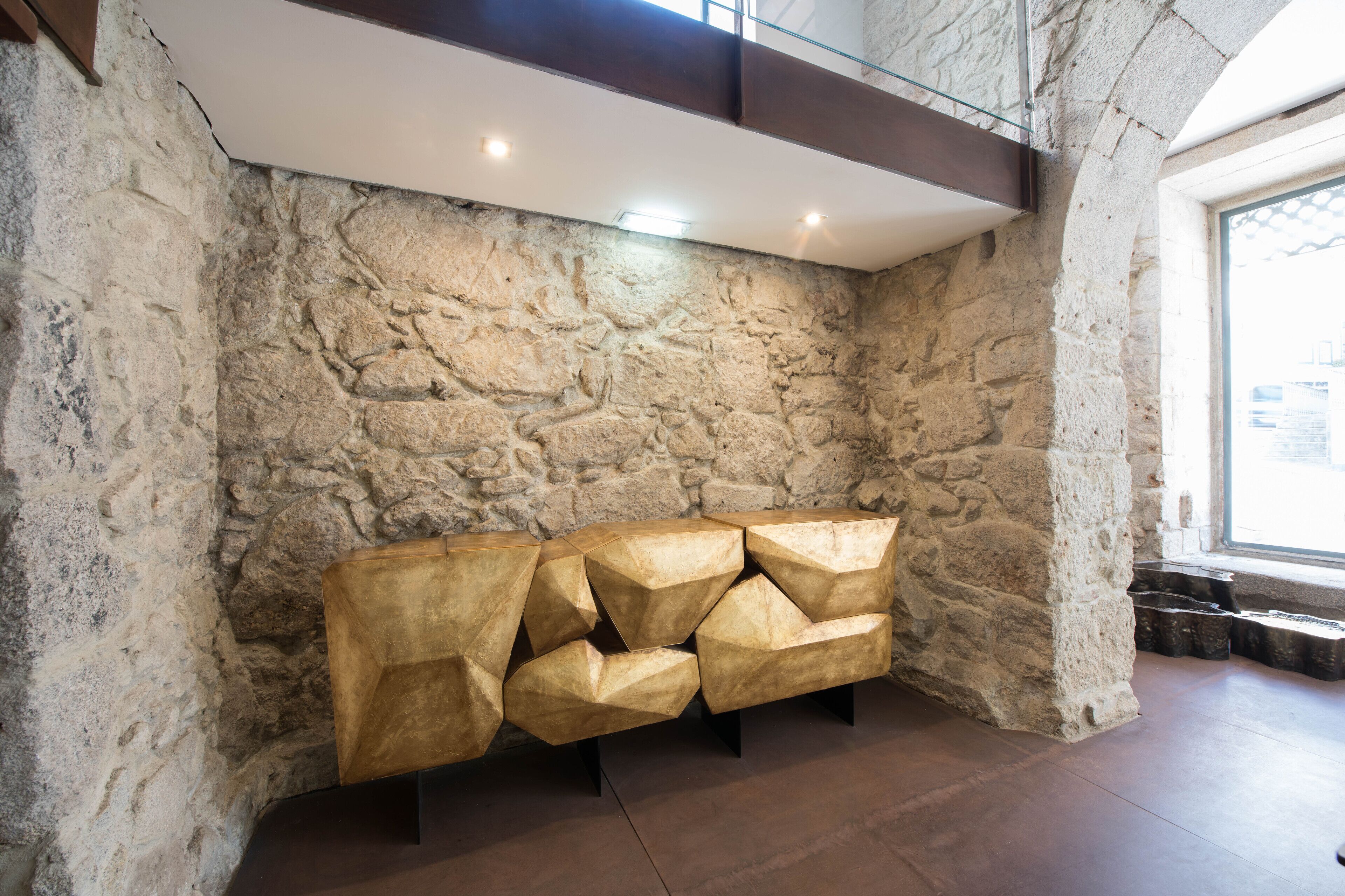 A stone wall with a geometric wooden bench in a modern interior.