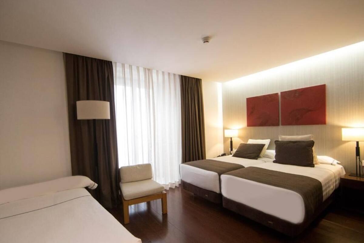 A hotel room with two beds, a chair, and a desk.