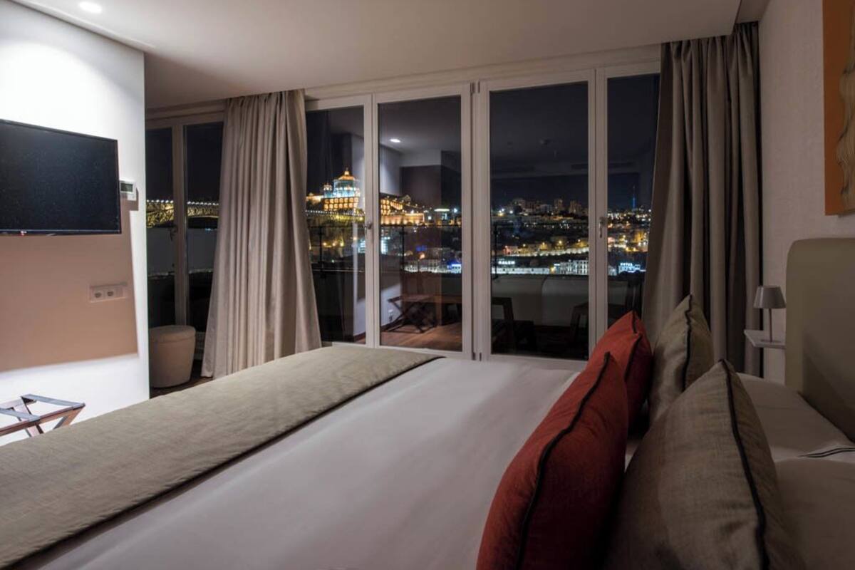 A hotel room with a large bed, a TV, and a view of a cityscape at night.