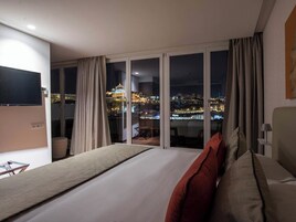 A hotel room with a large bed, a TV, and a view of a cityscape at night.
