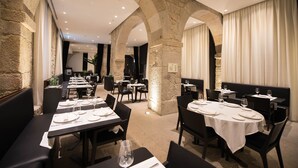A restaurant with stone arches, tables set with white tablecloths and wine glasses, and black chairs. - Hotel Carris Porto Ribeira (Porto)