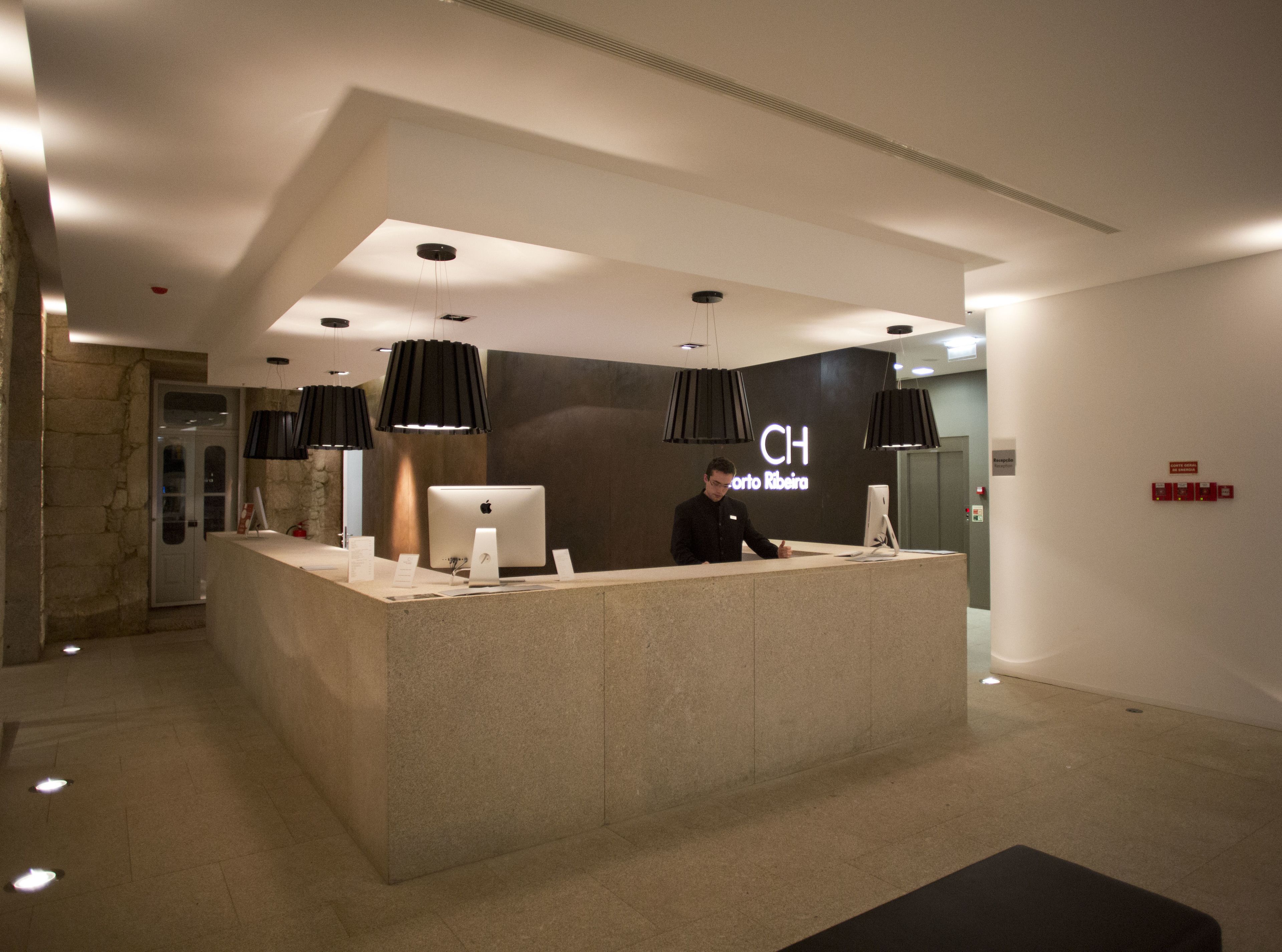 Un comptoir d’accueil au design moderne, doté d’un grand écran et d’un ordinateur. Des luminaires suspendus sont placés au-dessus du comptoir, et un panneau avec les initiales « CH » est fixé au mur.