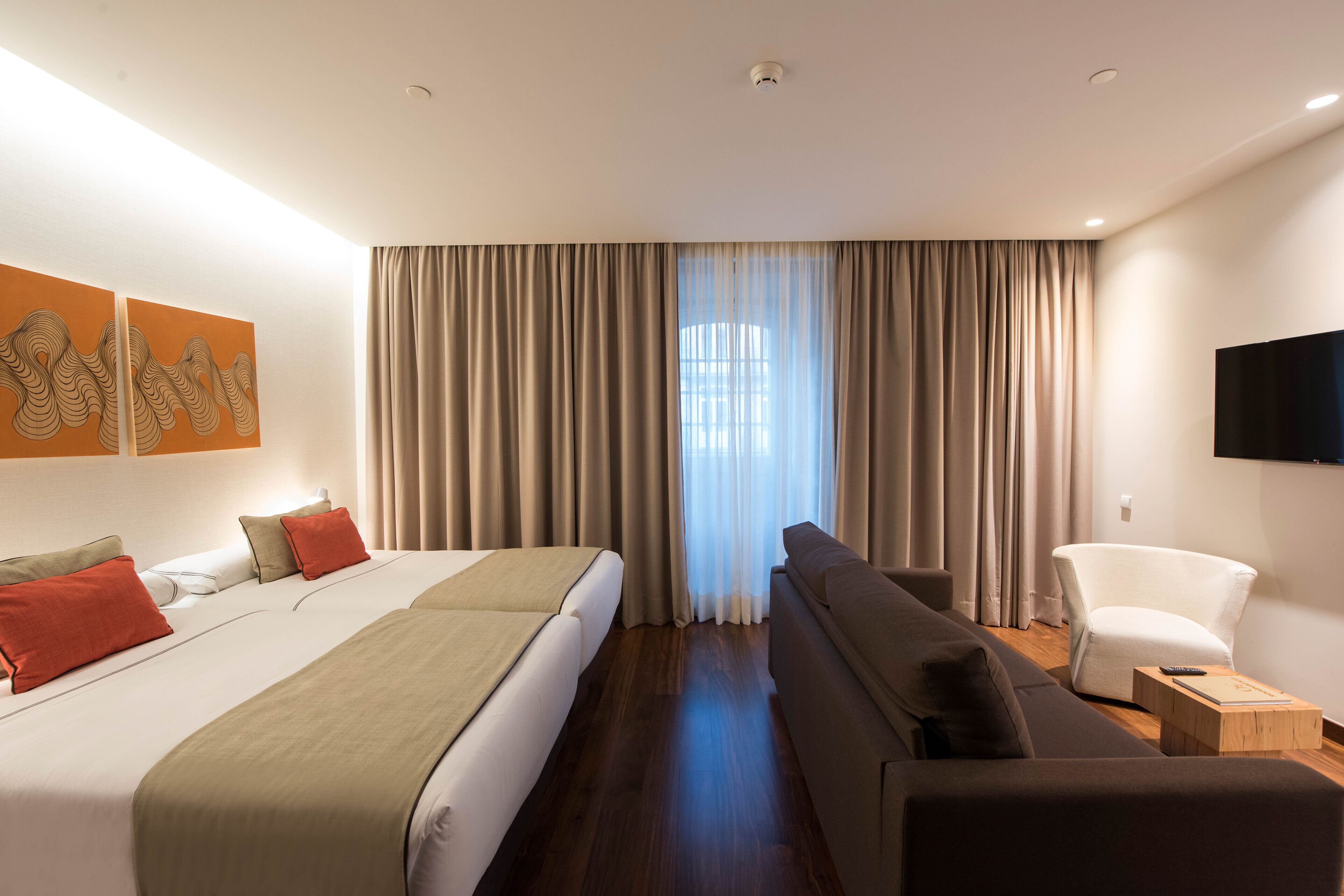 Una habitación de hotel moderna con una cama grande, un sofá, una silla y un televisor en la pared.