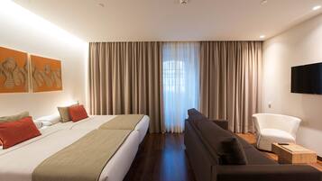 Una habitación de hotel moderna con una cama grande, un sofá, una silla y un televisor en la pared.