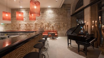 A bar area with a stone wall, a grand piano, and a red upholstered sofa.