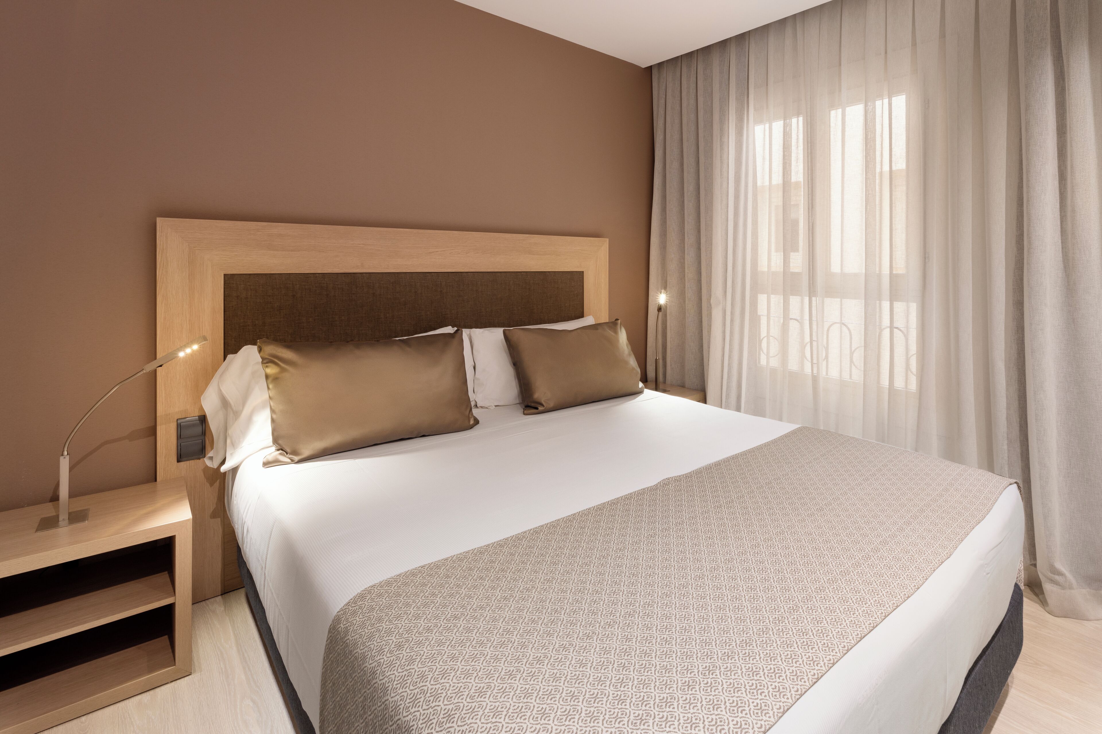 Un letto rifatto con cura, con copriletto decorato, una testiera in legno e un comodino con una lampada.