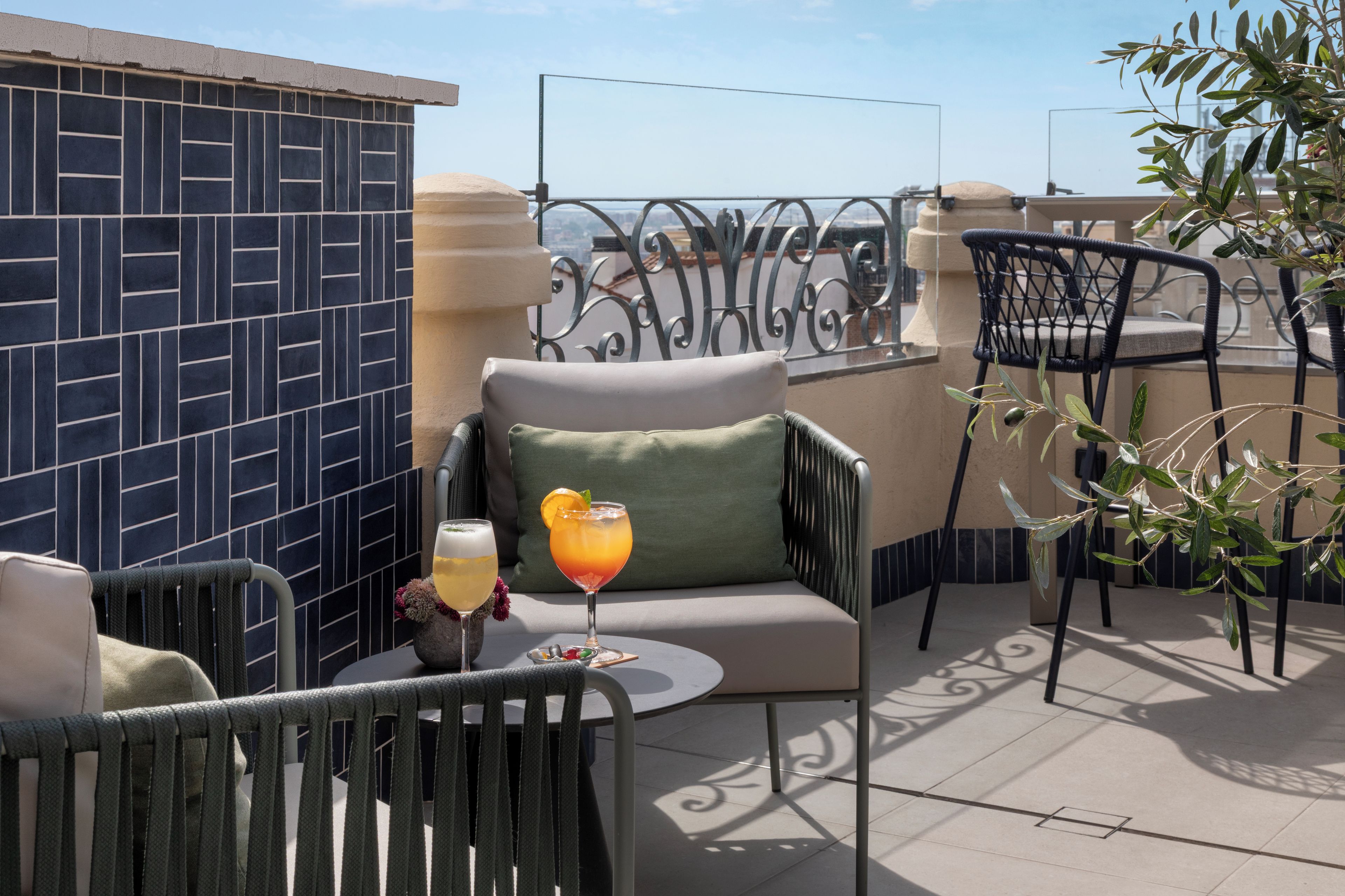 Eine Terrasse mit Sitzgelegenheit, zwei Getränken und Blick auf die Stadt.