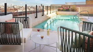 Zona de piscina en la azotea con vista a la ciudad, mesa de billar y dos sillas.