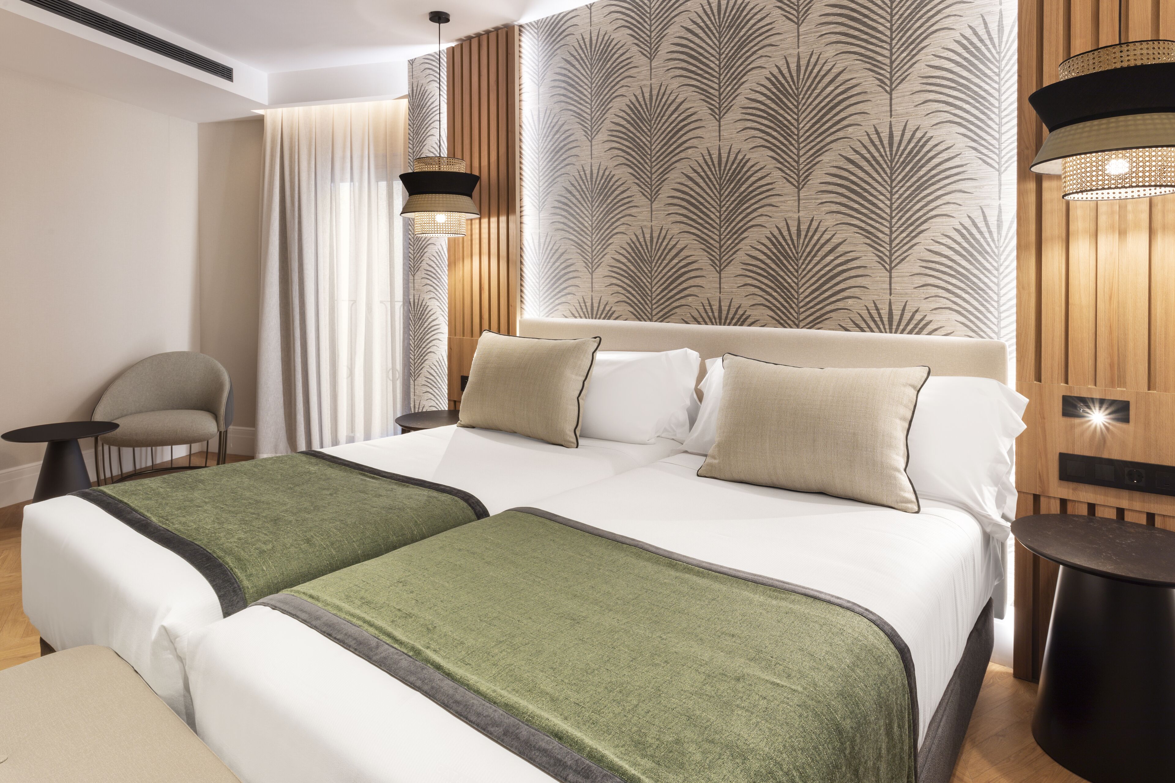 A hotel room with a large bed, two bedside tables, a chair, and a wall with a leaf pattern.