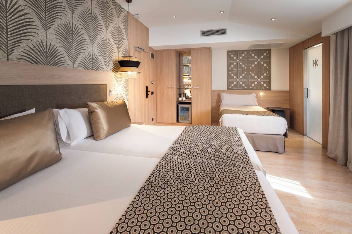 A hotel room with a large bed, a smaller bed, a wardrobe, a desk, and a bathroom.