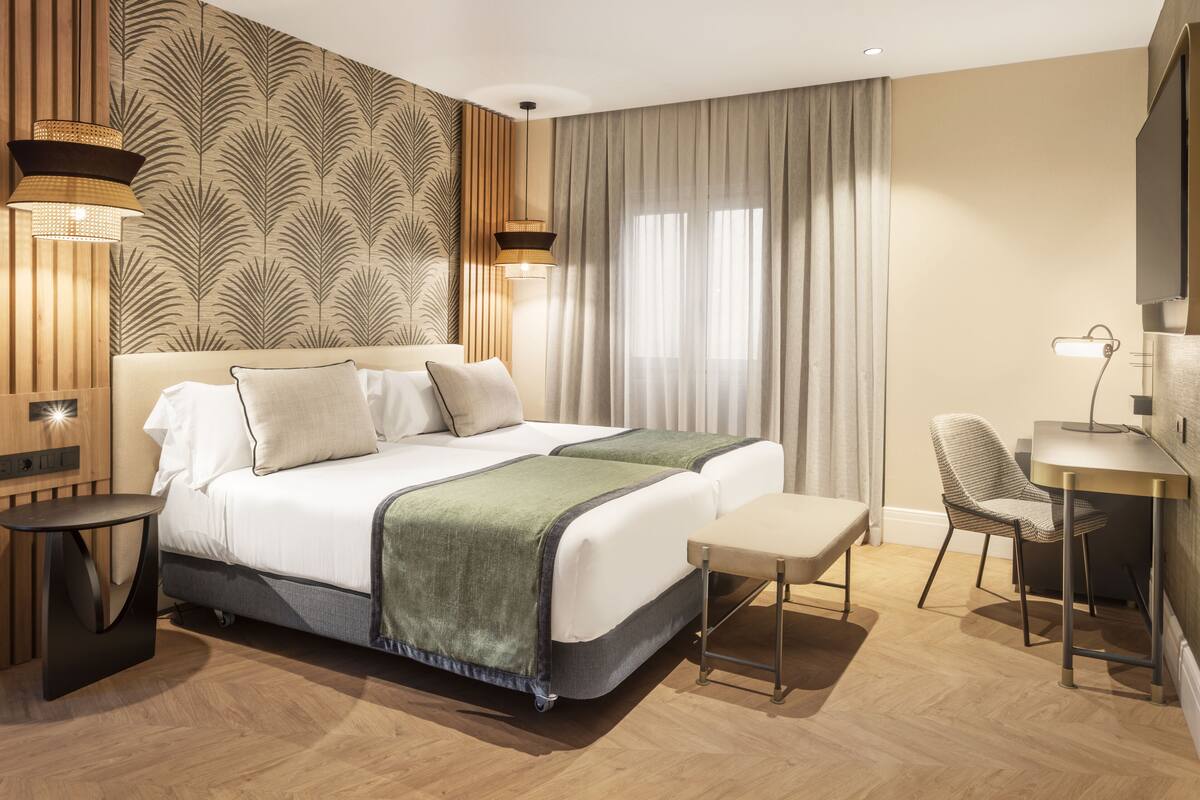 A modern hotel room with a large bed, bedside tables, a desk, and a chair.