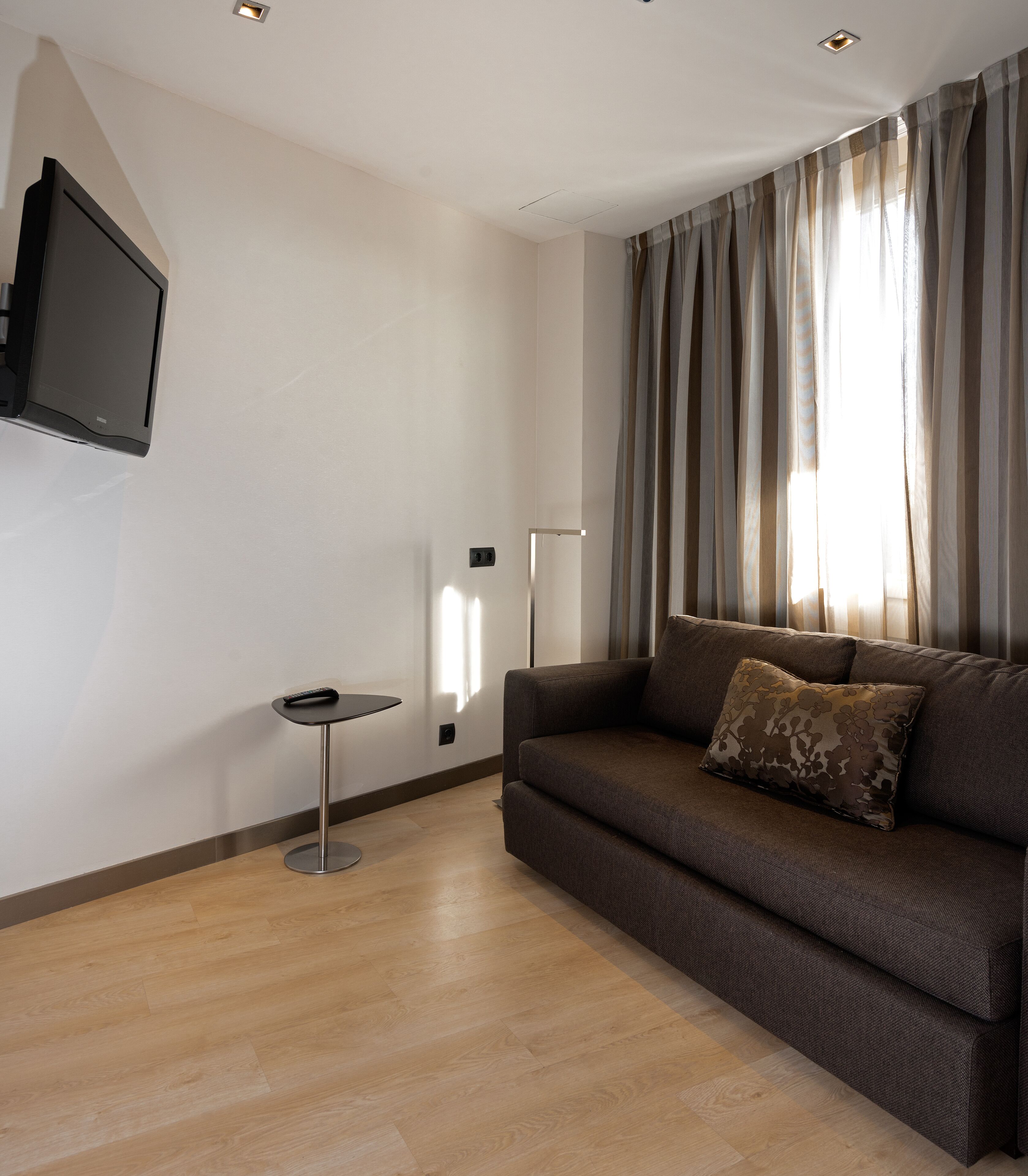 Ein modernes Wohnzimmer mit braunem Sofa, einem kleinen runden Tisch und einem an der Wand befestigten Fernseher.