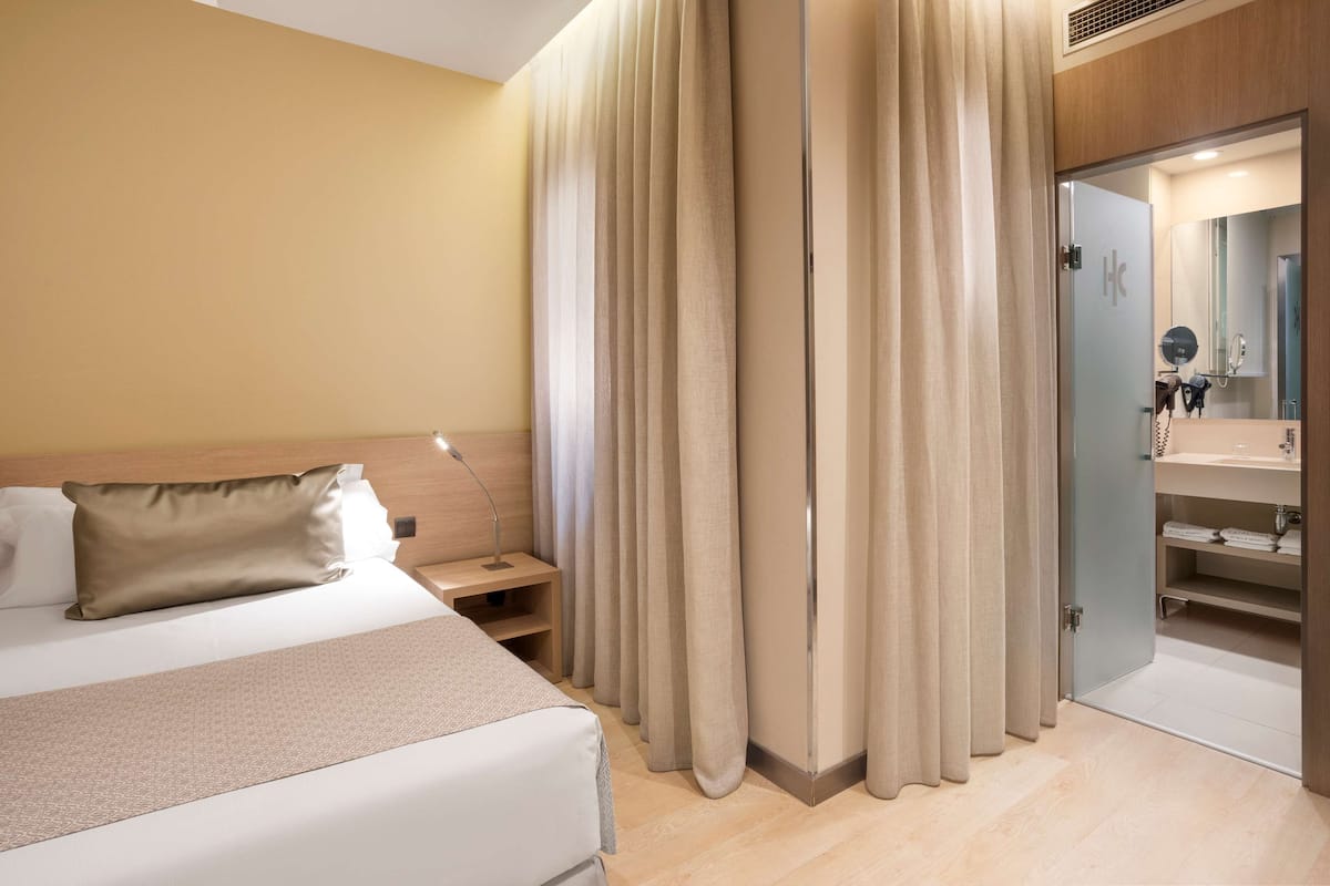 A hotel room with a bed, bedside table, and a bathroom visible through an open door.