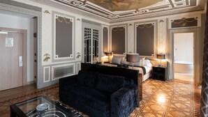 Una lujosa habitación de hotel con diseño clásico, que incluye una cama grande, un sofá azul oscuro y un techo decorativo.