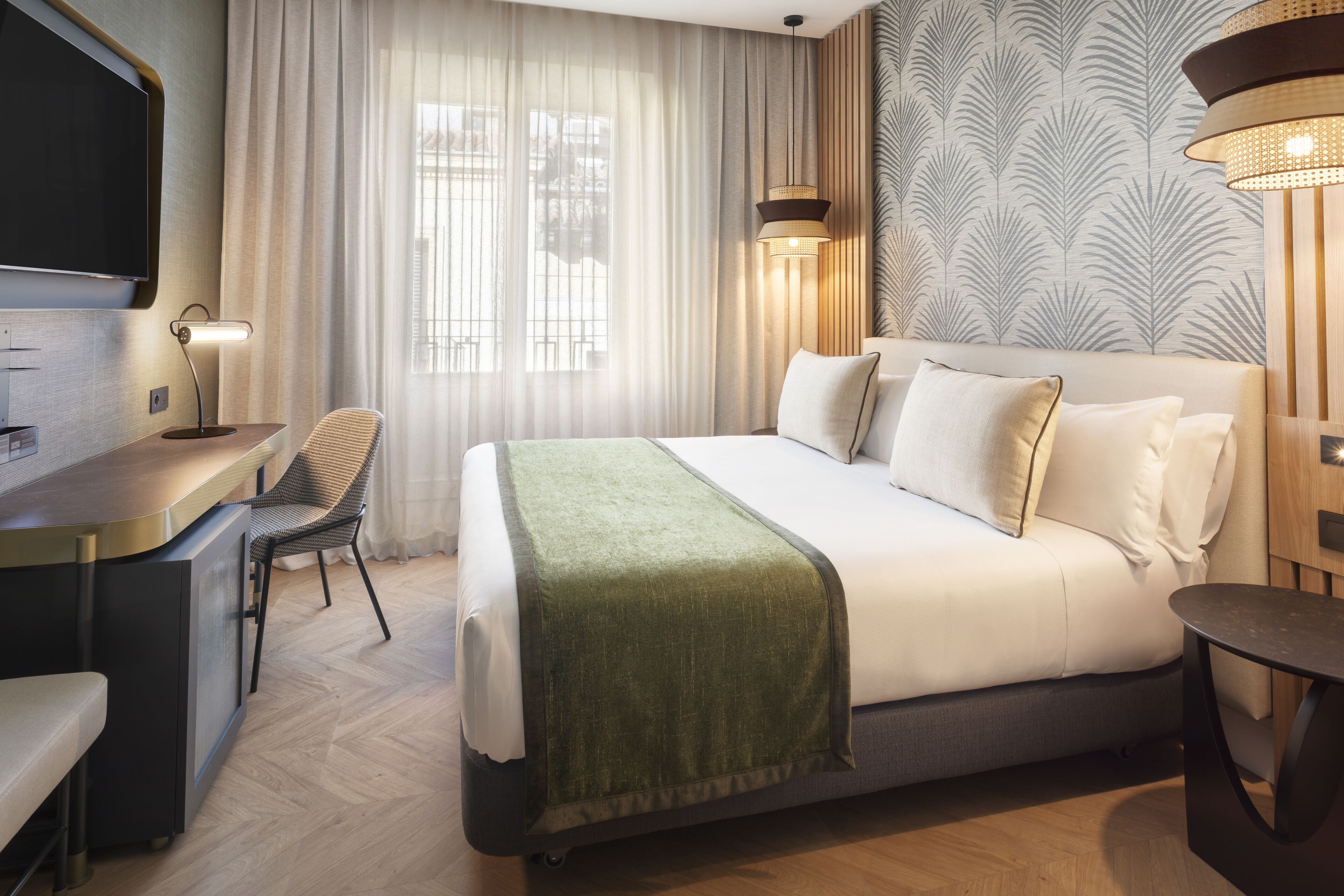Una habitació d'hotel moderna amb un llit, una taula de treball, una cadira i un televisor.
