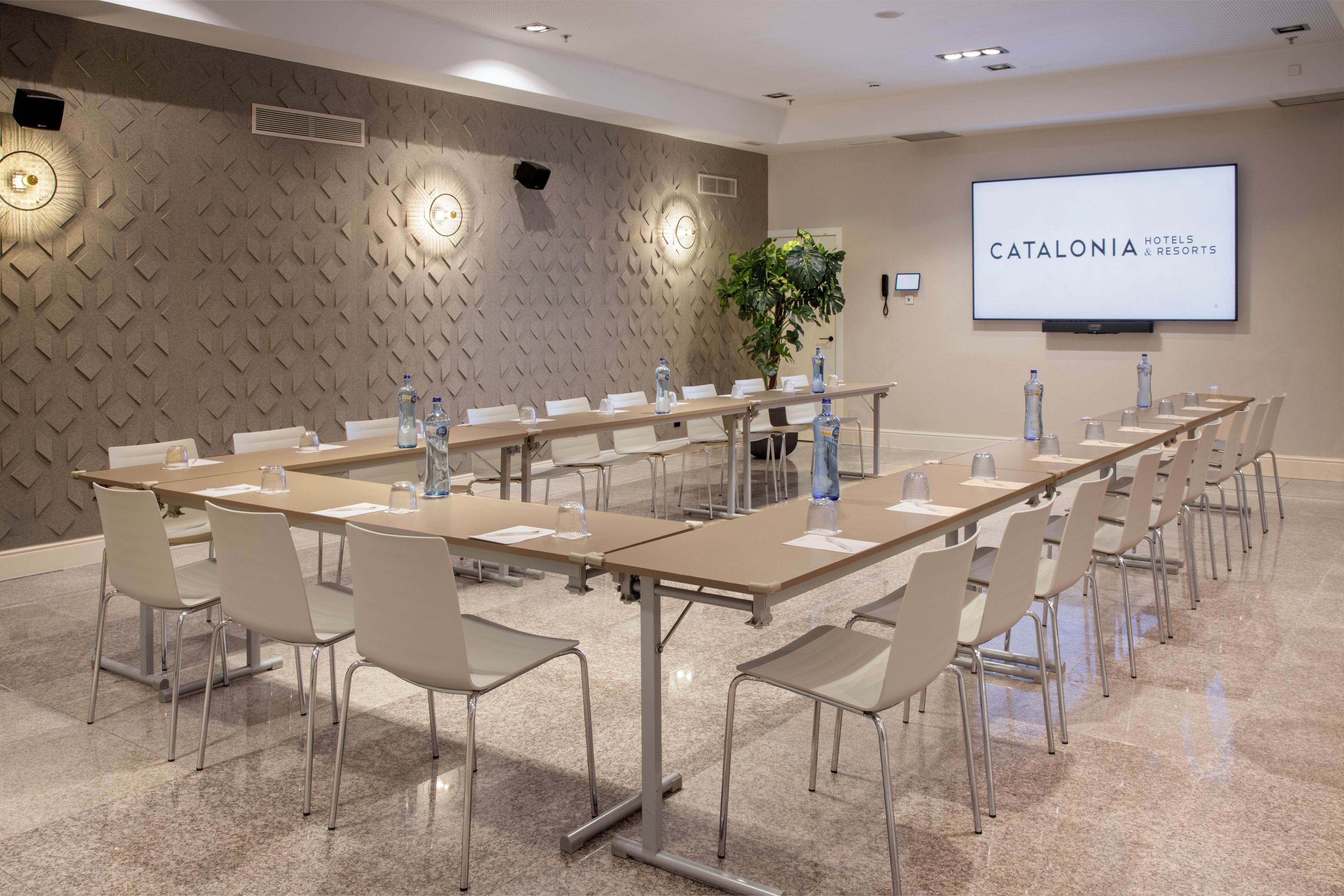 A conference room with a long table, chairs, a projector screen, and a plant.