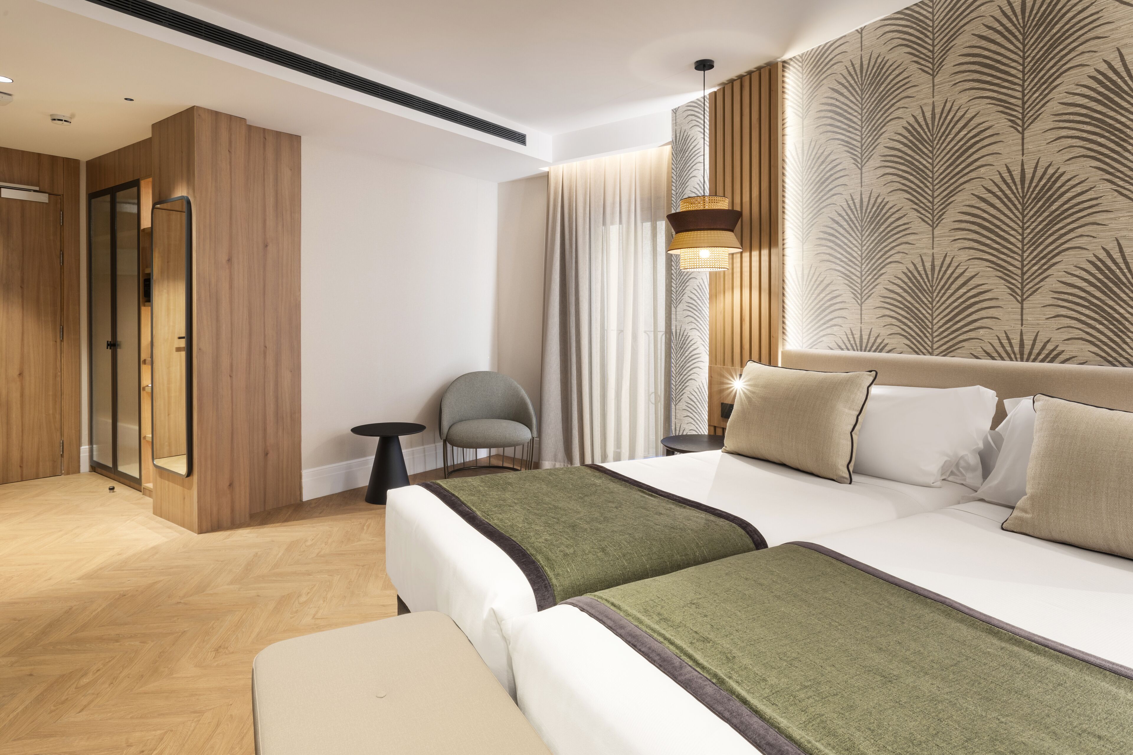 Ett modernt hotellrum med en stor säng, en sittgrupp med en stol, ett litet bord och en spegel.
