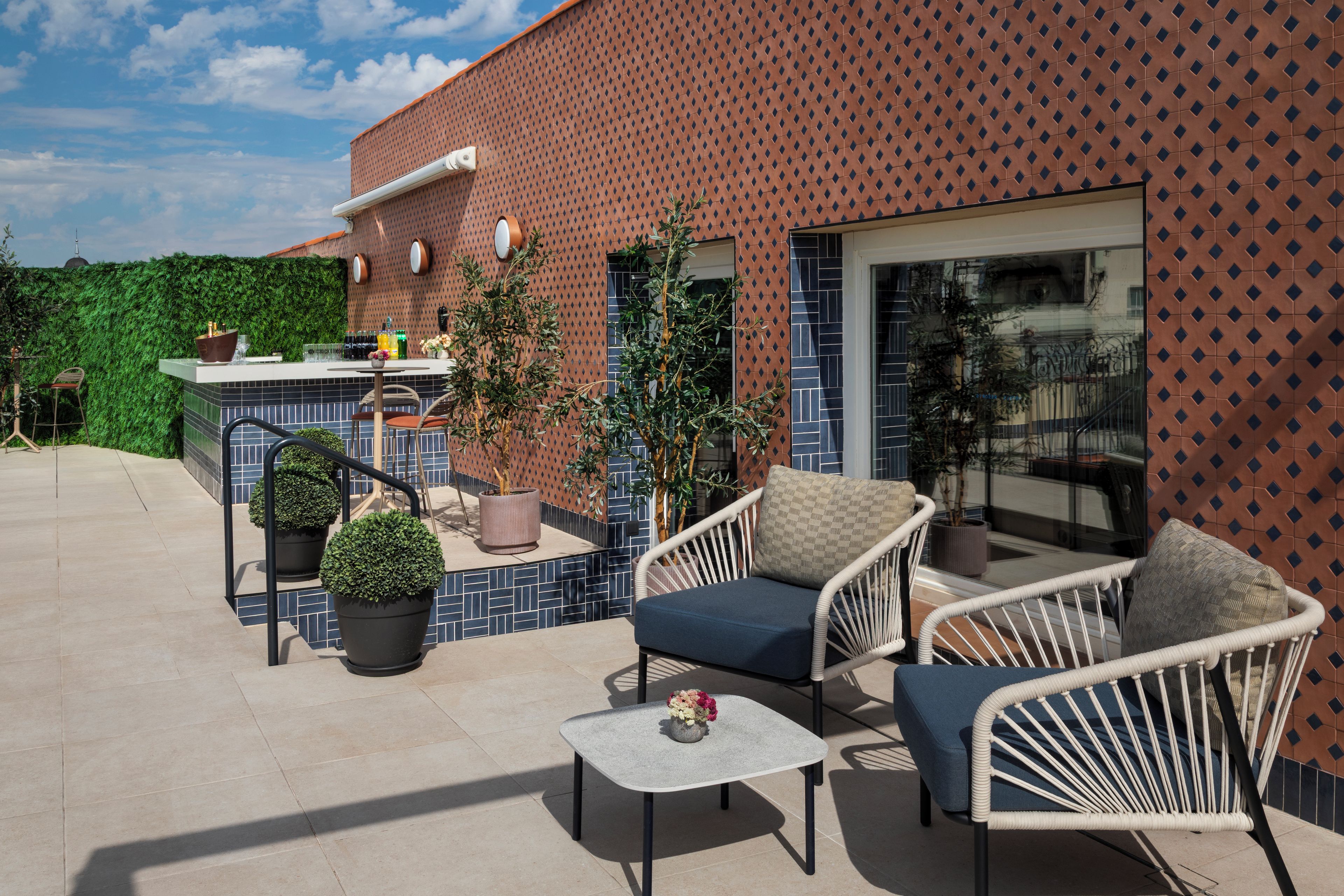 An outdoor patio area with a seating arrangement, a bar area, and a view of a building with a patterned facade.