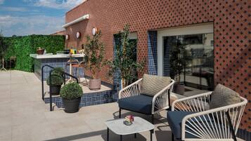Ein Außenbereich mit einer Terrasse, einer Sitzgruppe, einer Bar und Blick auf ein Gebäude mit einer verzierten Fassade.