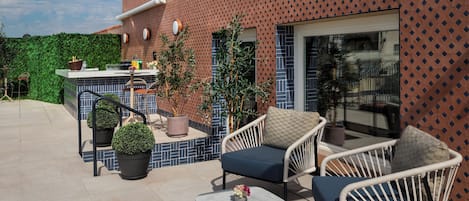 An outdoor patio area with a seating arrangement, a bar area, and a view of a building with a patterned facade.