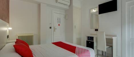 Habitación de hotel con cama, escritorio, silla, equipo de aire acondicionado, televisor y radiador.