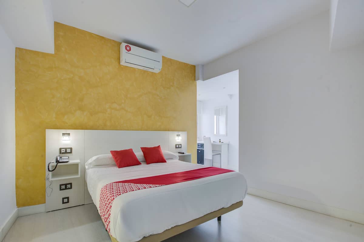 Une chambre d’hôtel moderne avec un grand lit, un téléphone sur la table de chevet et un petit bureau avec une chaise.