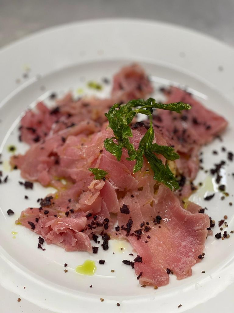 Un plato blanco con un guiso, adornado con hierbas y pimienta negra.