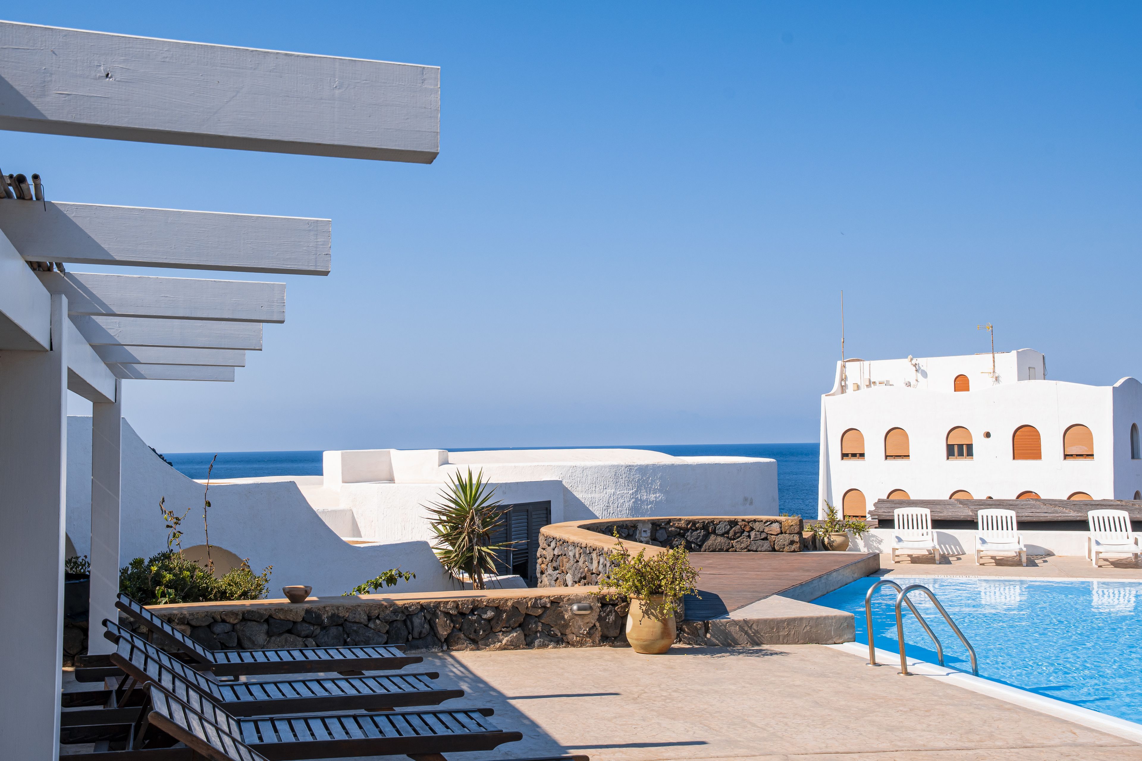 Zona de piscina con sillones de descanso, pared de piedra y vista al mar.