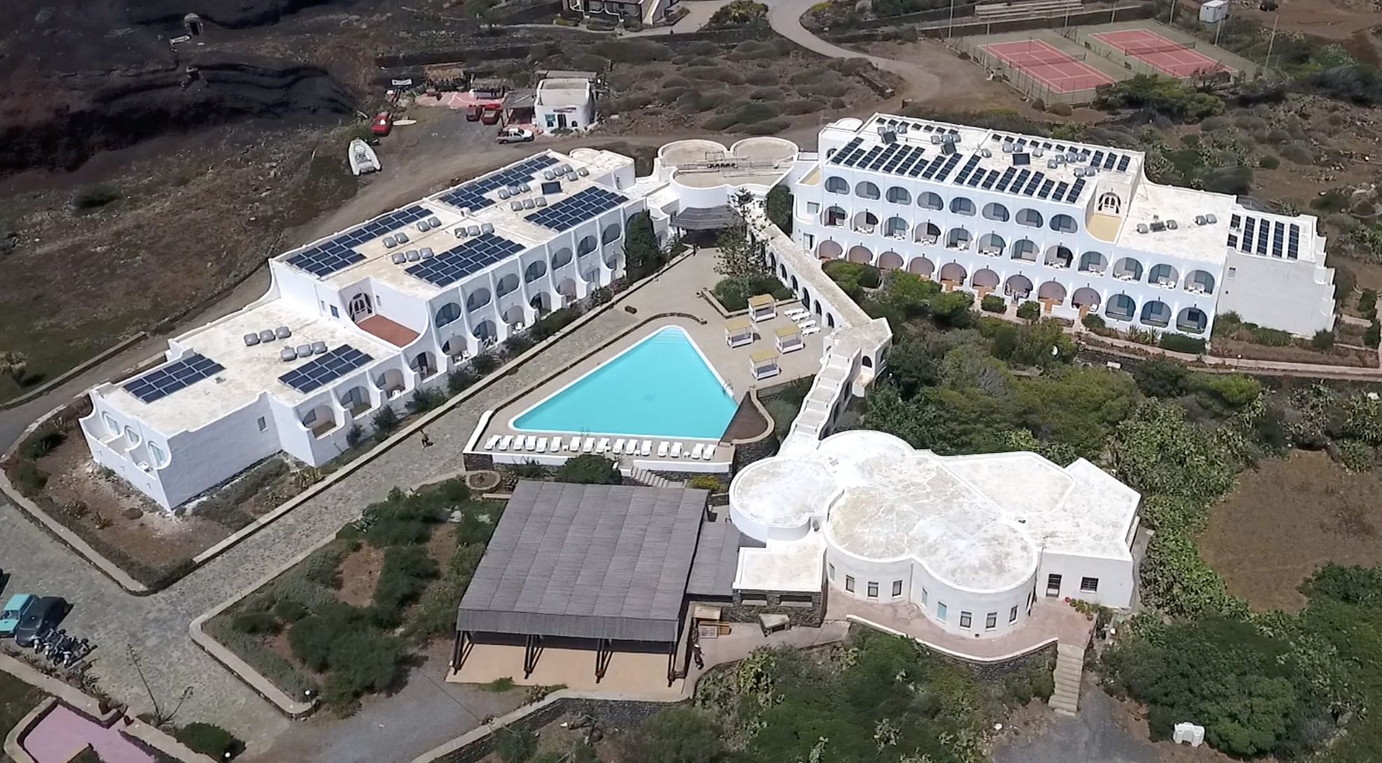 Vue aérienne d’un complexe hôtelier comprenant plusieurs bâtiments, une piscine et des panneaux solaires.