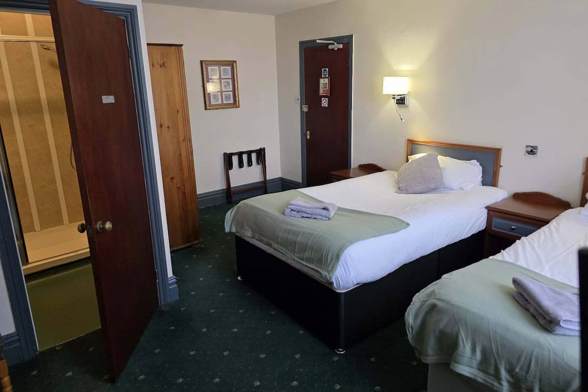 A hotel room with two beds, a wooden wardrobe, a small table, and a wall-mounted light.