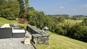 A stone bench with cushions and a lantern, overlooking a grassy landscape with trees and hills. - High Grassings Country House (Ambleside)
