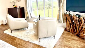 A modern living room with a large window, a white sofa, a coffee table, and a TV on a wooden stand. - High Grassings Country House (Ambleside)